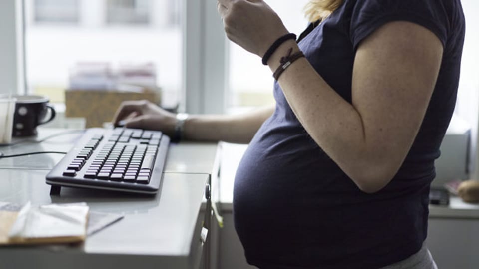 Symbolbild. Eine schwangere Frau steht vor ihrem Computer.