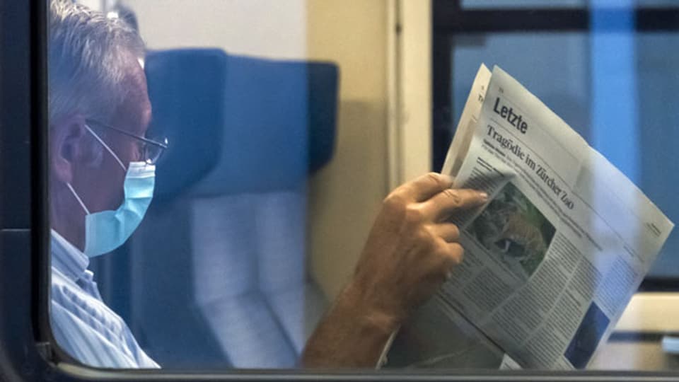 Reisender mit Schutzmaske beim Zeitungslesen. Symbolbild.
