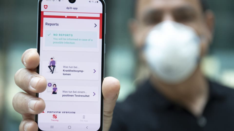 Ein Mann mit Schutzmaske zeigt ein Handy mit der Swiss Covid App