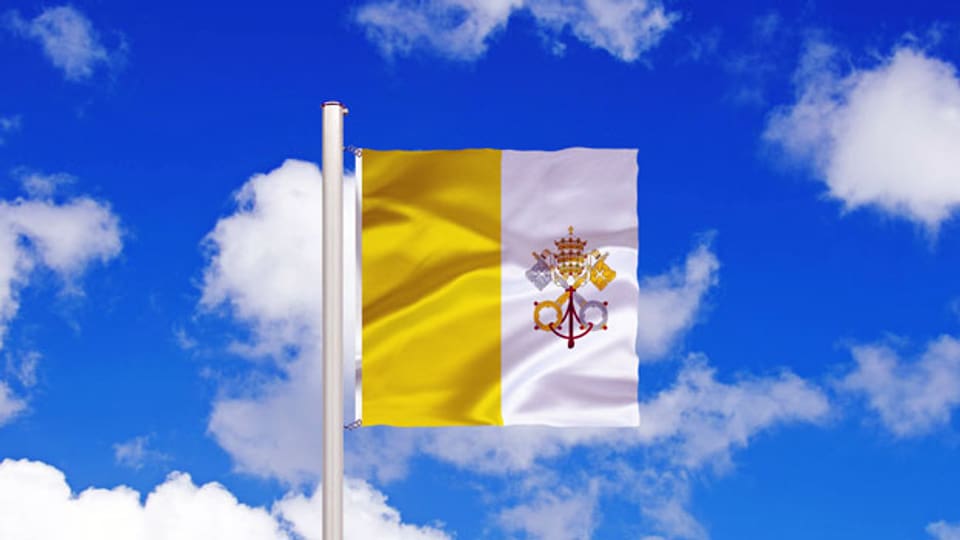 Die Fahne von Vatikan flackert vor blauem Wolkenhimmel.
