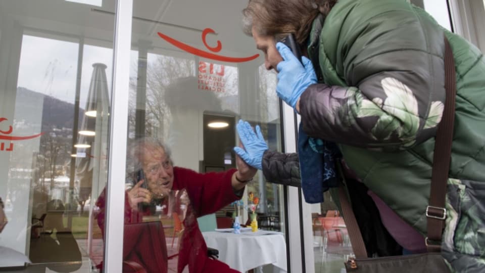 Monica telefoniert durch eine Scheibe mit ihrer 88-jährigen Mutter Giuseppina, am Mittwoch, 1. April 2020, im Altersheim Serena in Lugano. Aufgrund des Coronavirus wird ein direkter Kontakt vermieden.