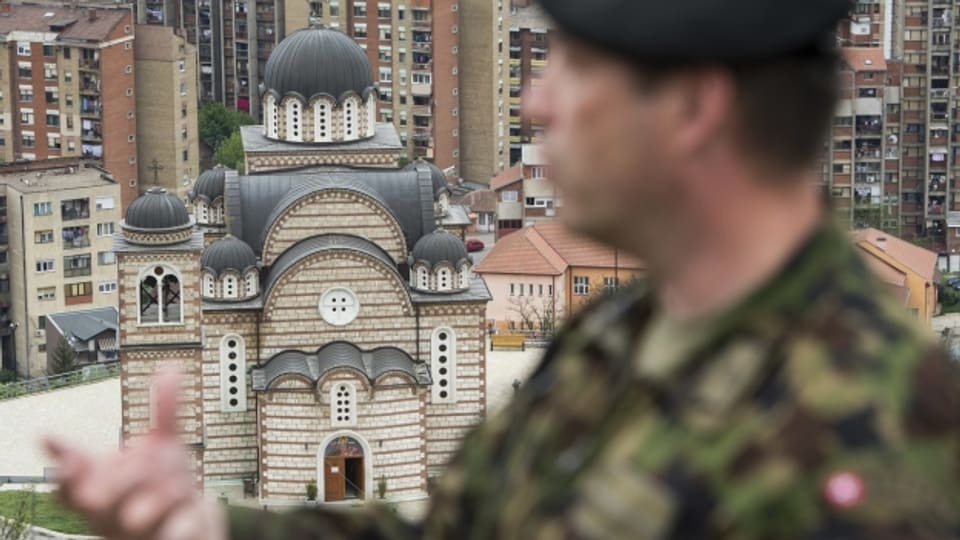 Schweizer Militärangehöriger steht auf einer Anhöhe. Im Hintergrund ist eine Moschee