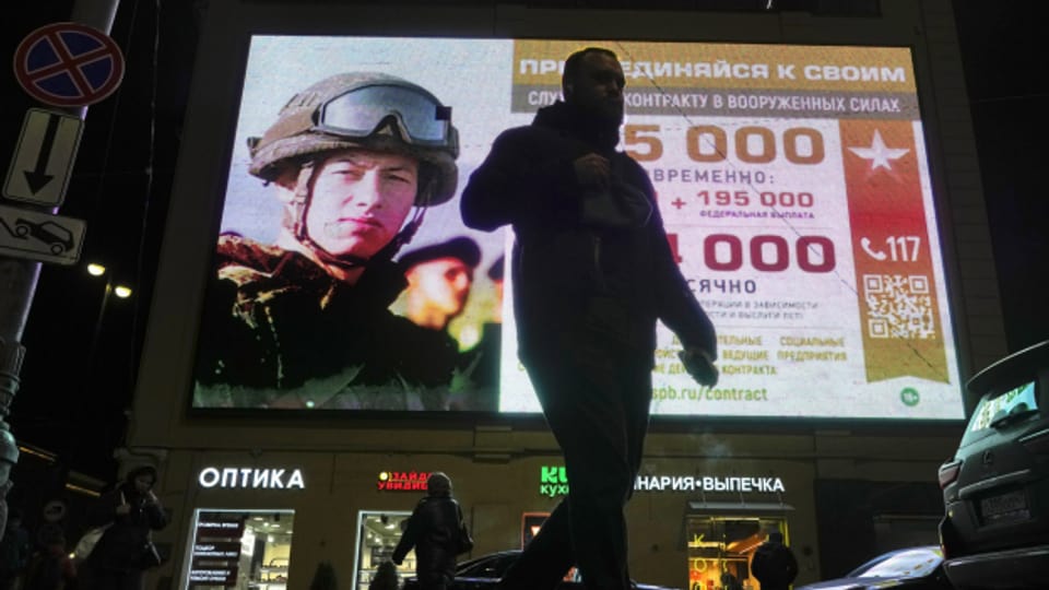 Ein Mann geht am Montag in St. Petersburg, Russland, an einem Werbebildschirm vorbei, auf dem Soldaten der russischen Armee abgebildet sind.