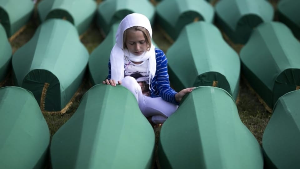Ein Mädchen kniet vor Särgen der Opfer von Srebrenica