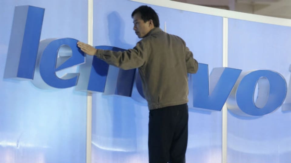 Ein Chinesischer Arbeit befestigt ein Lenovo Schild an einer IT-Messe.