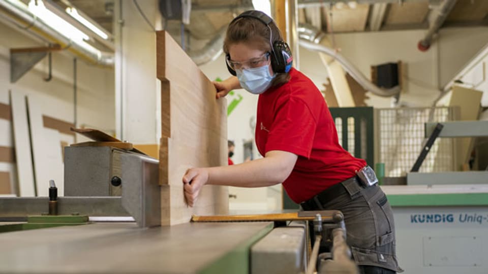 Eine lernende Schreinerin bearbeitet eine Holzplatte mit einer Hobelmaschine.