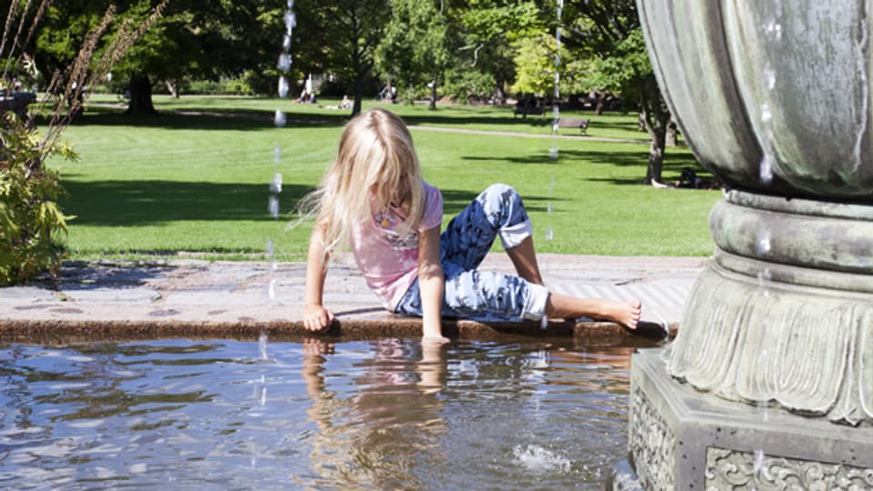 Mädchen verschafft sich Abkühlung am Springbrunnen.