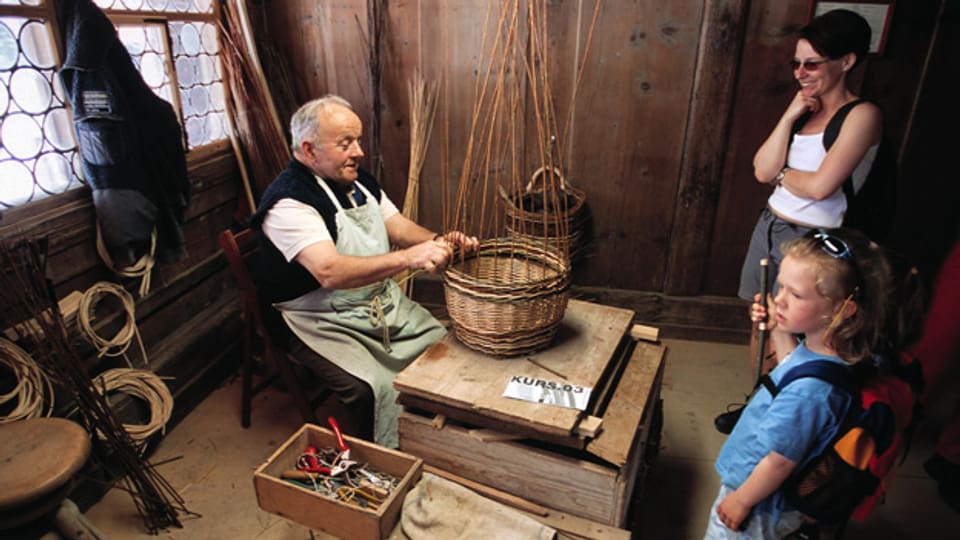 Im Freilichtmuseum Ballenberg wird bis heute traditionelles Handwerk demonstriert. In der Aufnahme von 2003 schauen zwei Gäste einem Korbflechter bei seiner Tätigkeit zu.