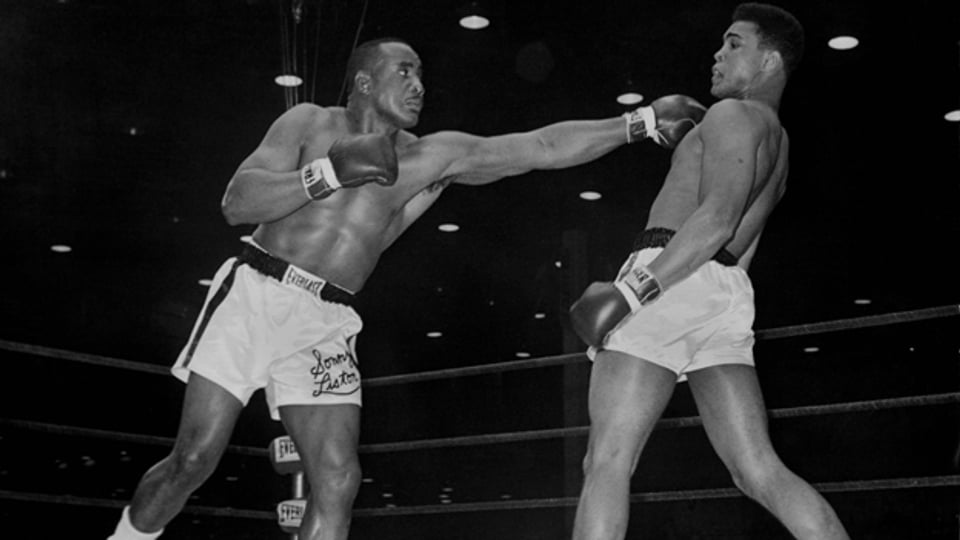 Cassius Clay weicht einer Linken von Sonny Liston elegant aus. Der Schwergewichtskampf am 25. Februar 1964 in Miami endet mit einer Sensation: Der für unbezwingbar gehaltene Sonny Liston verliert gegen Cassius Clay durch technisches K.O. in der 7. Runde.