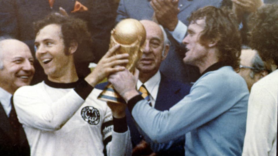 Die Bundesrepublik Deutschland wird 1974 an der Fussball-Welmeisterschaft im eigenen Land Weltmeister. Nach dem 2:1 Sieg über Holland nehmen Franz Beckenbauer und Sepp Maier den Pokal entgegen.