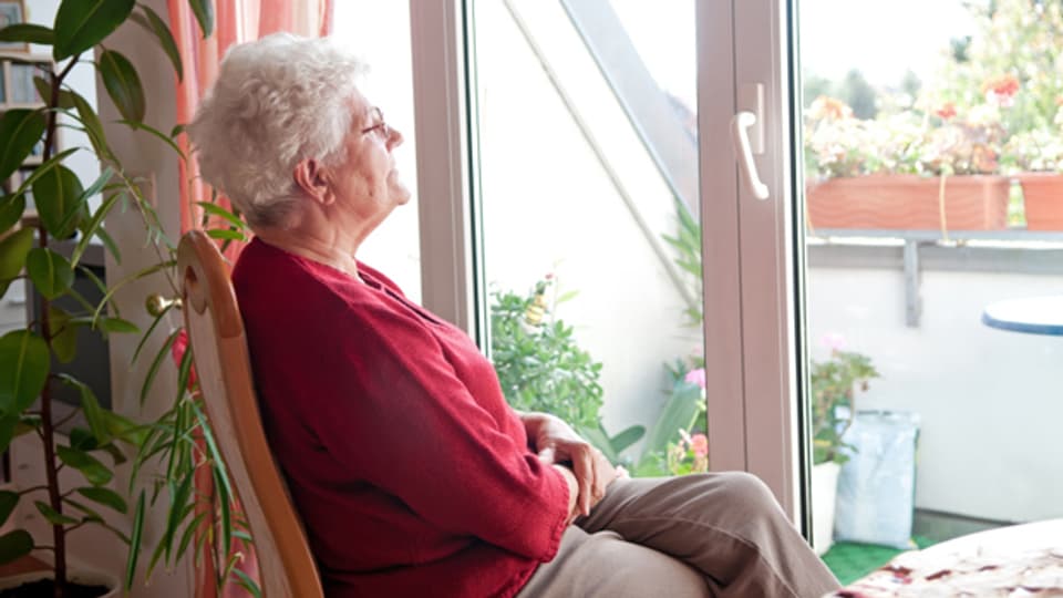 Eine Seniorin sitzt auf einem Stuhl und starrt aus dem Fenster.