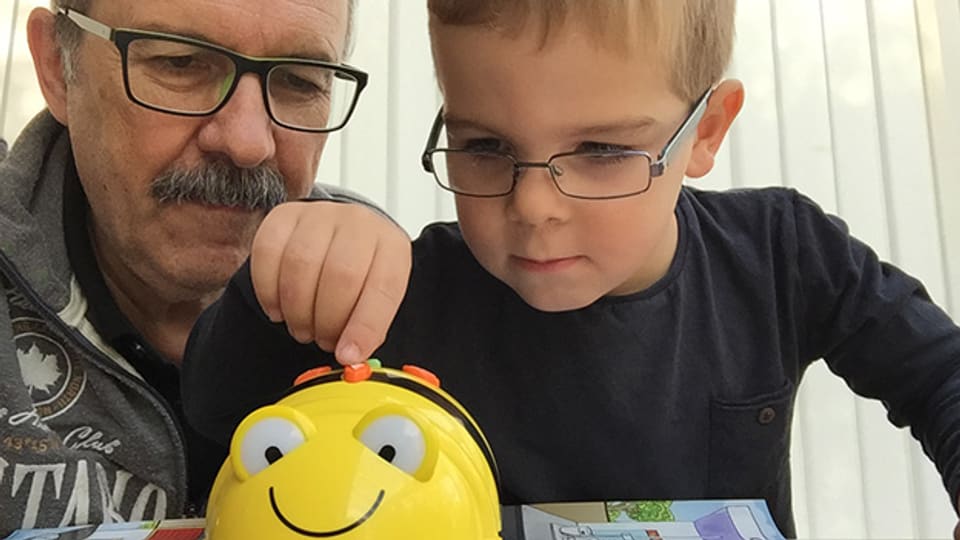 Grossvater und Enkel spielen gemeinsam mit dem Bee-Bot, einem programmmierbaren Spiel-Roboter.
