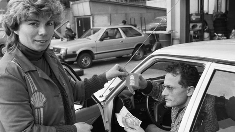 Eine Tankwartin verkauft einem Automobilisten eine Autobahnvignette, die ab 1. Januar 1985 obligatorisch ist, aufgenommen im Dezember 1984.