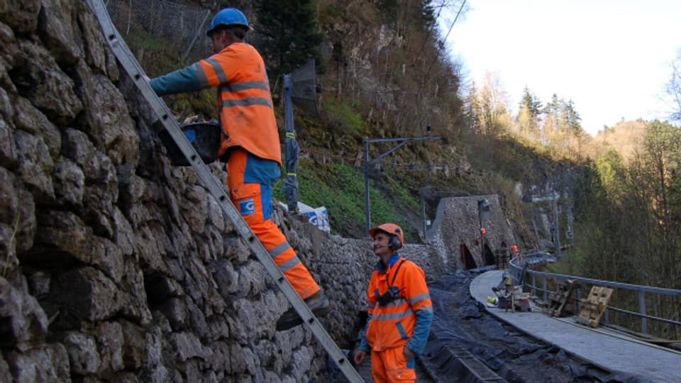 Zwei Arbeiter in Schutzanzügen sanieren eine Natursteinmauer.