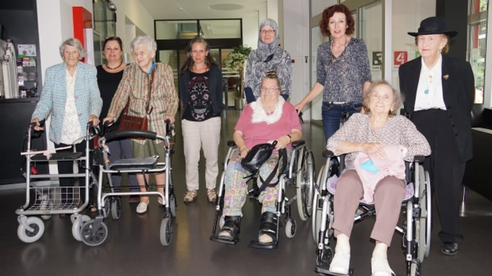 Fünf Damen im Rollstuhl, mit Gehstock oder Rollator und ihre Begleiterinnen.