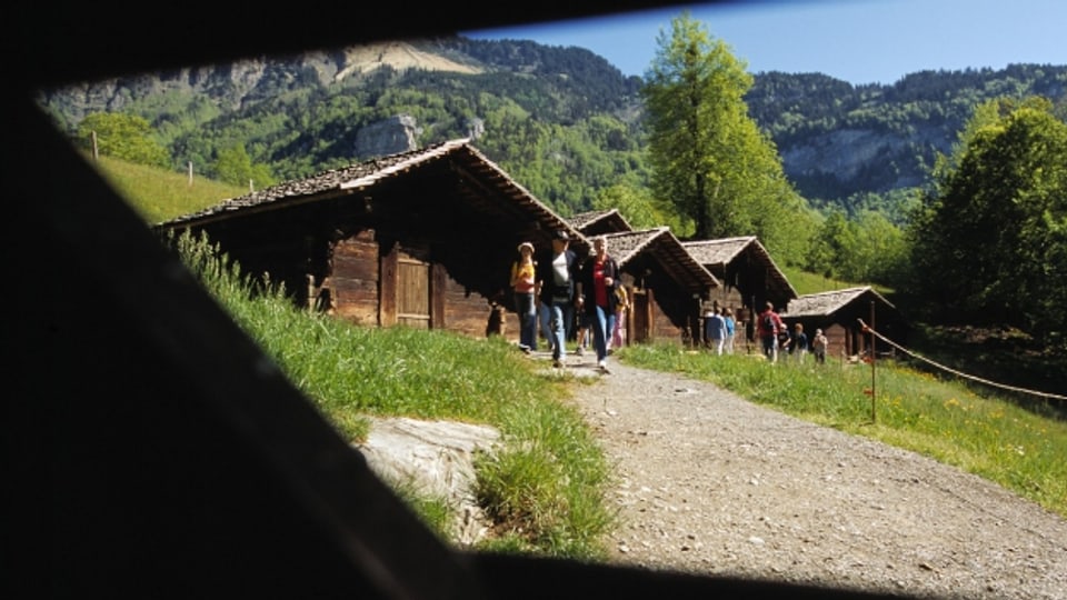 Besucher des Freilichtmuseums Ballenberg spazieren bei den Alpställen und Sennhütten aus Richinen/Bellwald vorbei.