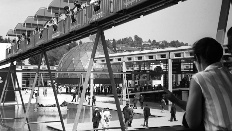 Besucherinnen und Besucher unterwegs an der Expo 64 auf der «Monorail». Die Schweizerische Landesausstellung dauerte vom 30. April 1964 bis zum 25. Oktober 1964.