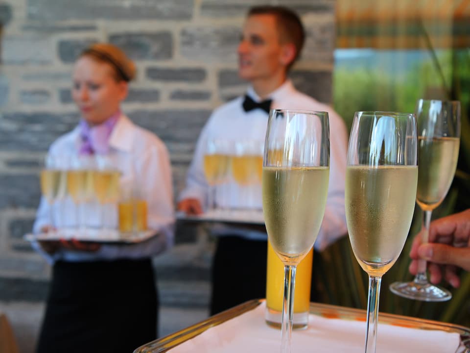 Champagnergläser im Vordergrund, im Hintergrund bringen Angestellte Nachschub