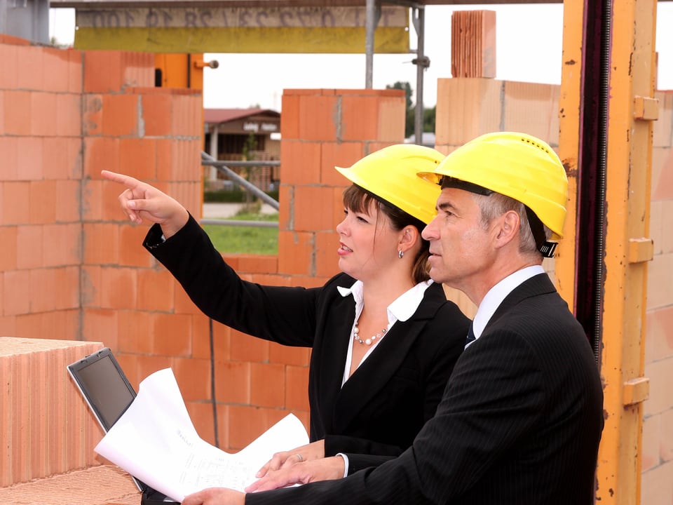 Architektin und Polier auf einer Baustelle mit Bauplan in der Hand. 