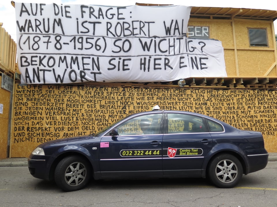 Taxi vor der Spanplattenwand mit Texten von Walser