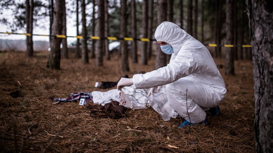 ein Kriminalbeamter in Onverall begutachtet eine Leiche im Wald
