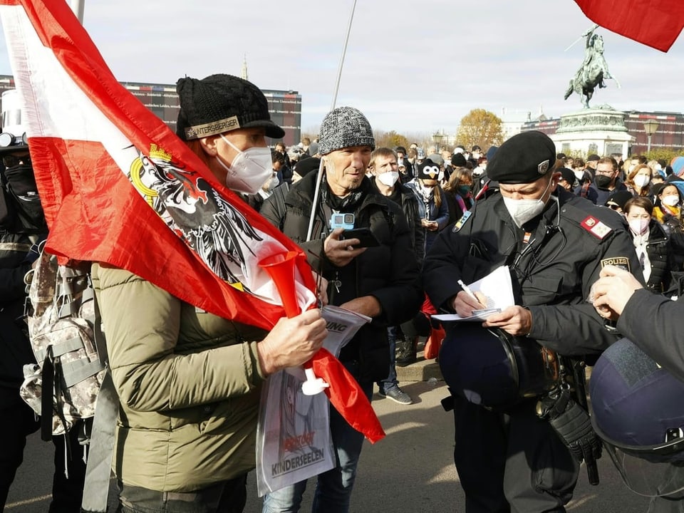 Zwei Polizisten stehen neben zwei Demonstranten. Ein Polizist schreibt auf einen Zettel.