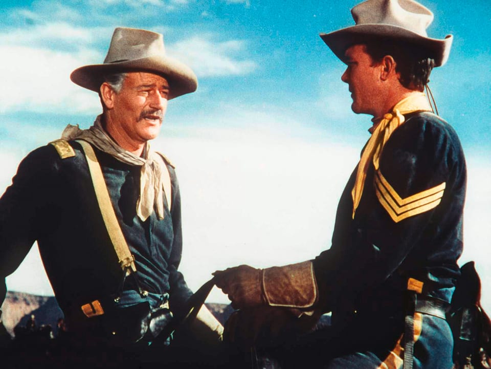 John Wayne und John Agar, beide auf einem Pferd, miteinander sprechend.