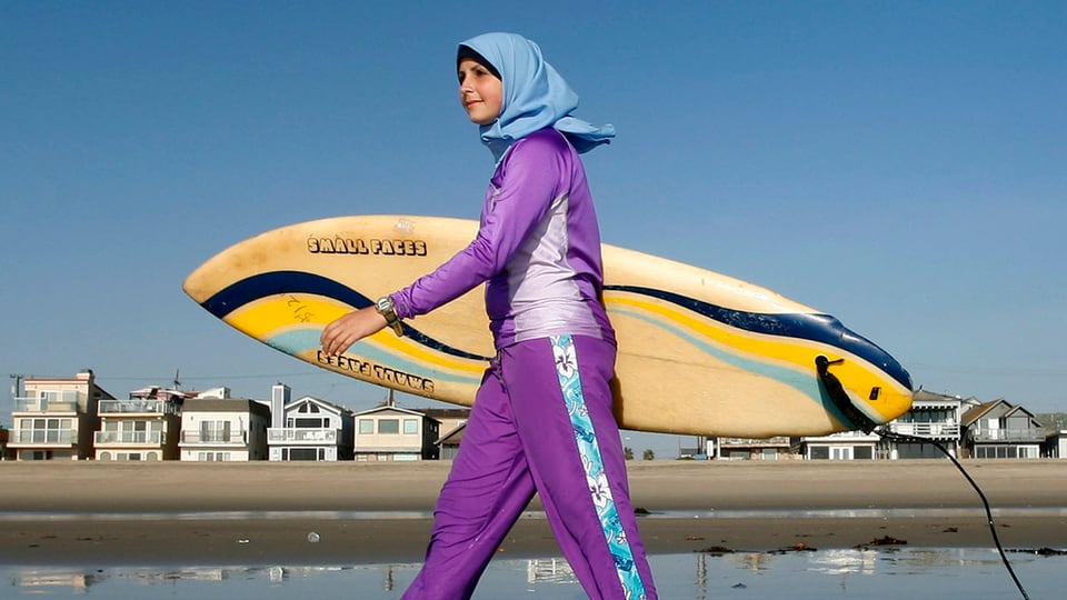 Muslima spaziert in einem violett-blauen Burkini am Strand von Newport in Kalifornien, der Anzug bedeckt ihren ganzen Körper, mit Ausnahme der Füsse, Hände und des Gesichts.