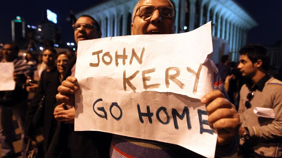 Ein Mann hält ein Plakat: John Kerry, geh nachhause.