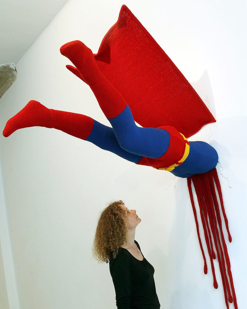 Superman in einer Kunstgalerie: Seine Beine ragen aus der Wand, stilisiertes Blut läuft herunter.