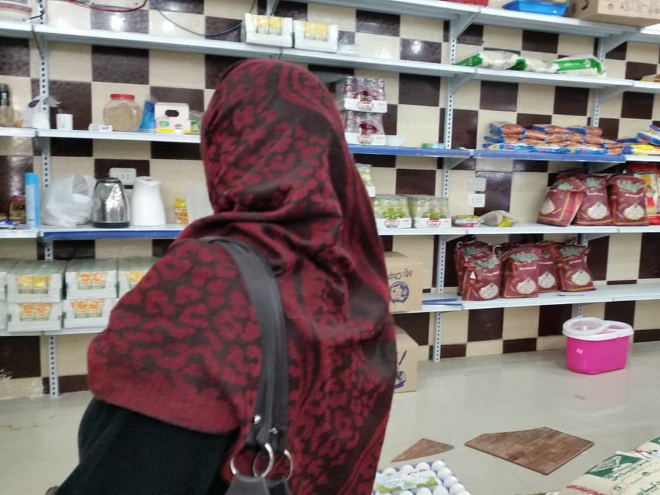 Frau mit Kopftuch steht vor Ladenregal. 