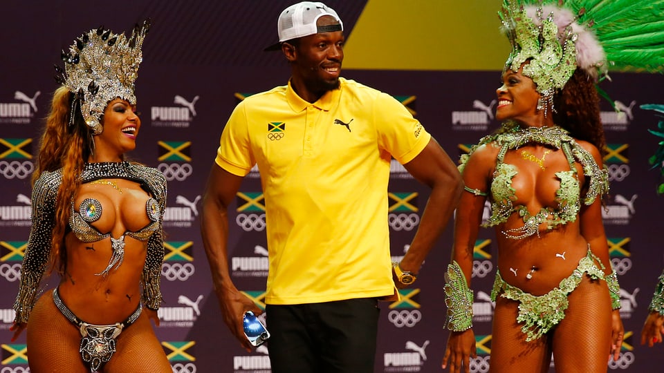 Usain Bolt umrahmt von zwei Sambatänzerinnen.