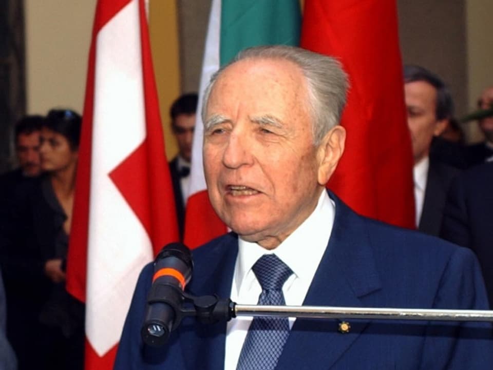 Carlo Azeglio Ciampi am Mikrofon. Im Hintergrund die Schweizer Flagge.