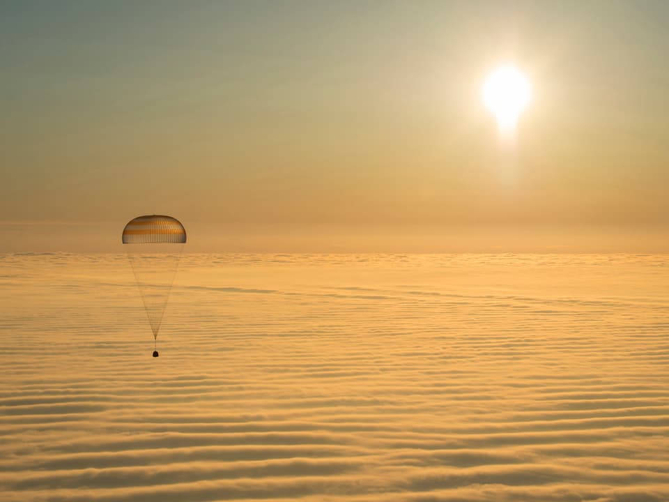 Eine Kapsel, die an einem Fallschirm hängt, gleitet Richtung Erde