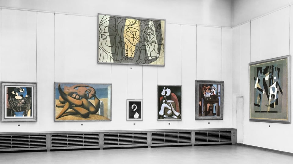An einer Wand in einem Museum hängen sieben Gemälde des Malers Picasso.