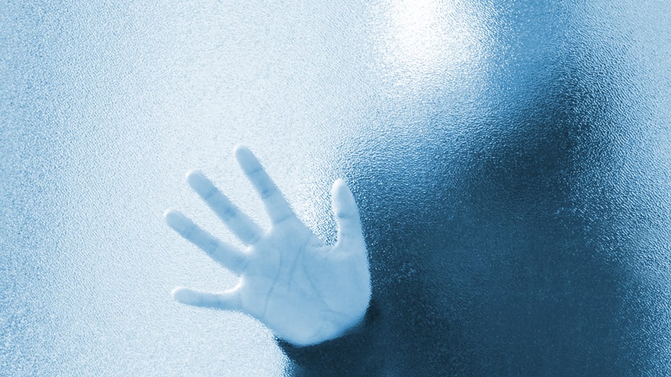 Eine Hand einer unbekannten Person an einer Fensterscheibe.