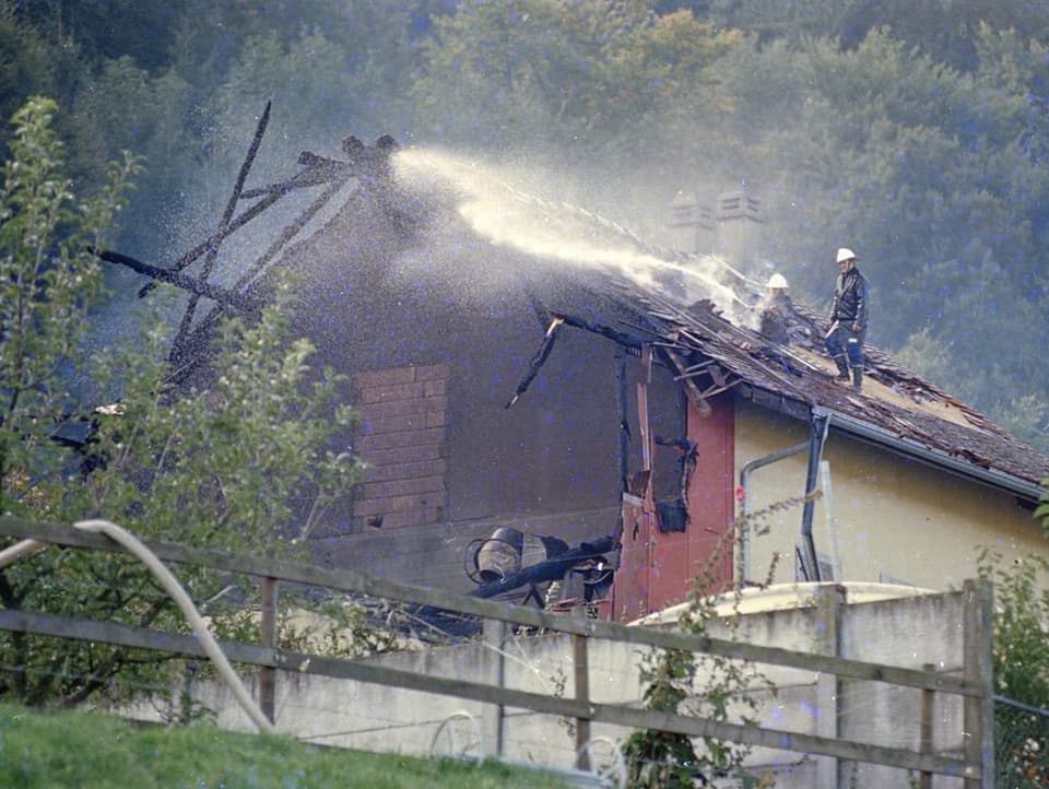 Feuerwehrleute stehen auf einem abgebrannten Schale und löschen einen Brand