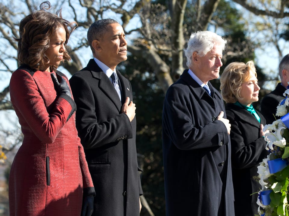Von links nach rechts: Michelle Obama, Barack Obama, Bill Clinton, Hillary Clinton bei einer Gedenkfeier, jeder mit der Hand auf dem Herzen
