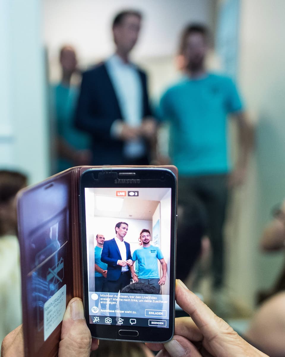 Durch einen Smartphone-Bildschirm sieht man Sebastian Kurz mit einem jungen Mann sprechen.
