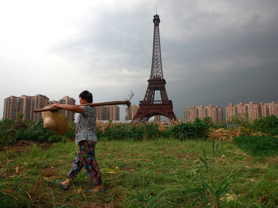 Chinesische Bäuerin vor Eiffelturm-Kopie, im Hintergrund Wohnblocks.