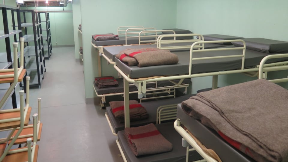 Bunkermässiges Zimmer mit Doppelstockbetten, auf denen Armeewolldecken liegen.