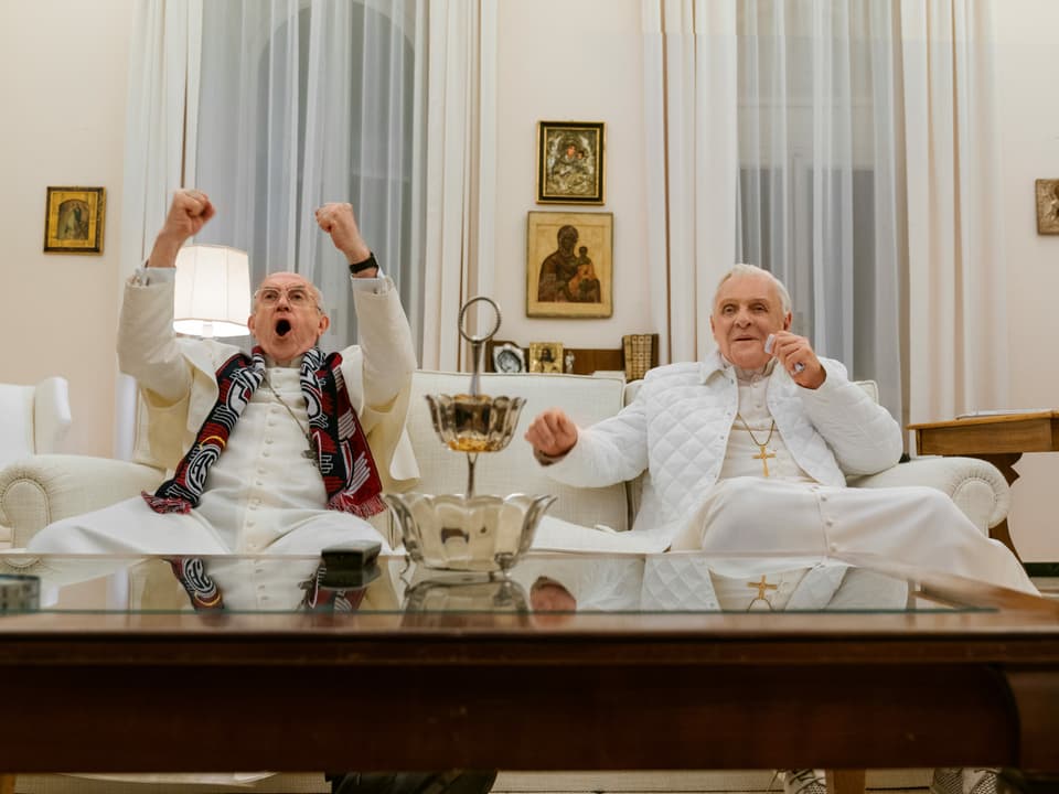 Zwei Päpste sitzten auf einem Sofa und jubeln.