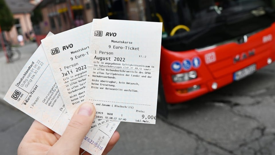 Eine Person hält 9-Euro-Tickets in der Hand. Im Hintergrund ist ein Bus.