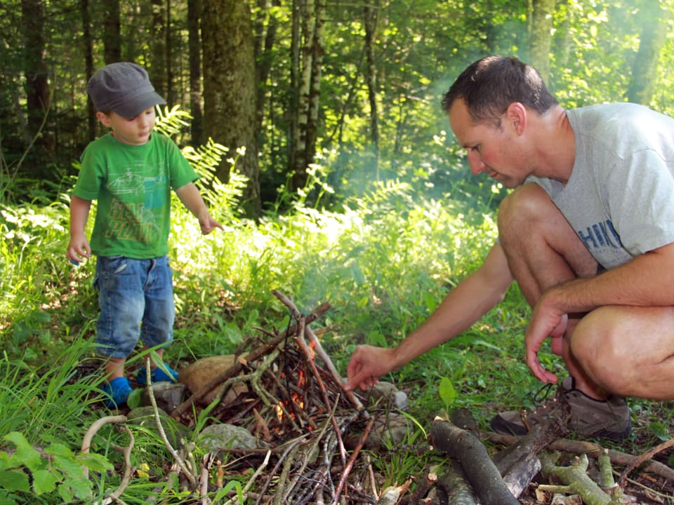 Kleiner Bub und Mann machen ein Feuer im Wald.