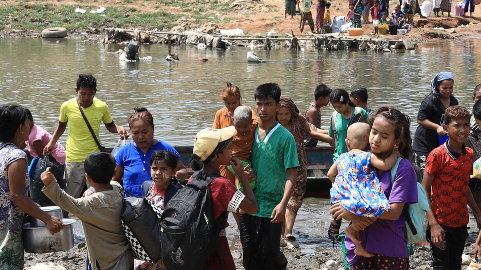 Eine Menschengruppe, die mit einem Boot einen Fluss überquert hat, auch mit Kleinkindern