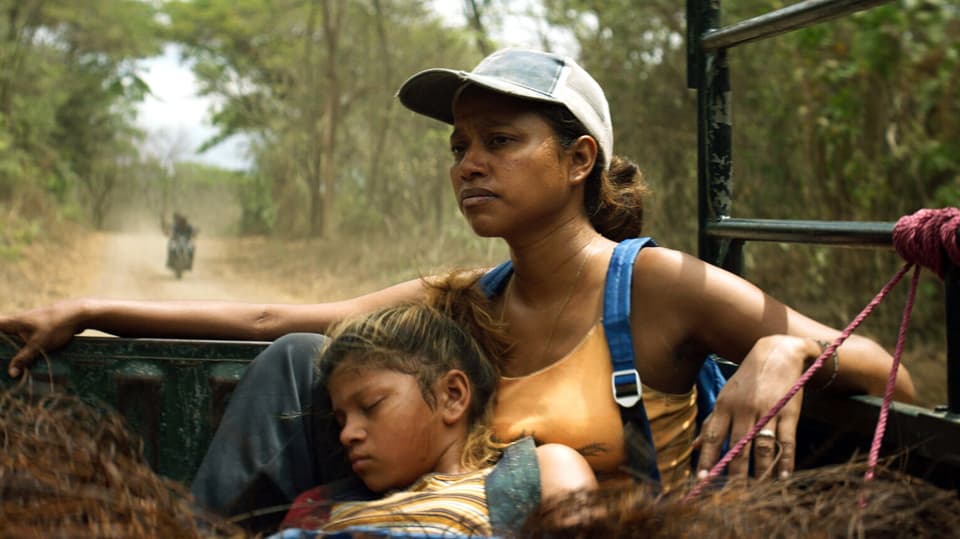 Eine Frau mit Cap sitzt auf einem Pick-up, an sie gelehnt schläft ein Mädchen.