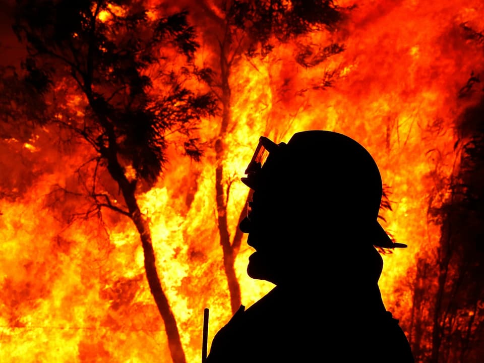 Feuerwehrmann als schwarze Silhouette vor brennendem Wald in Australien.