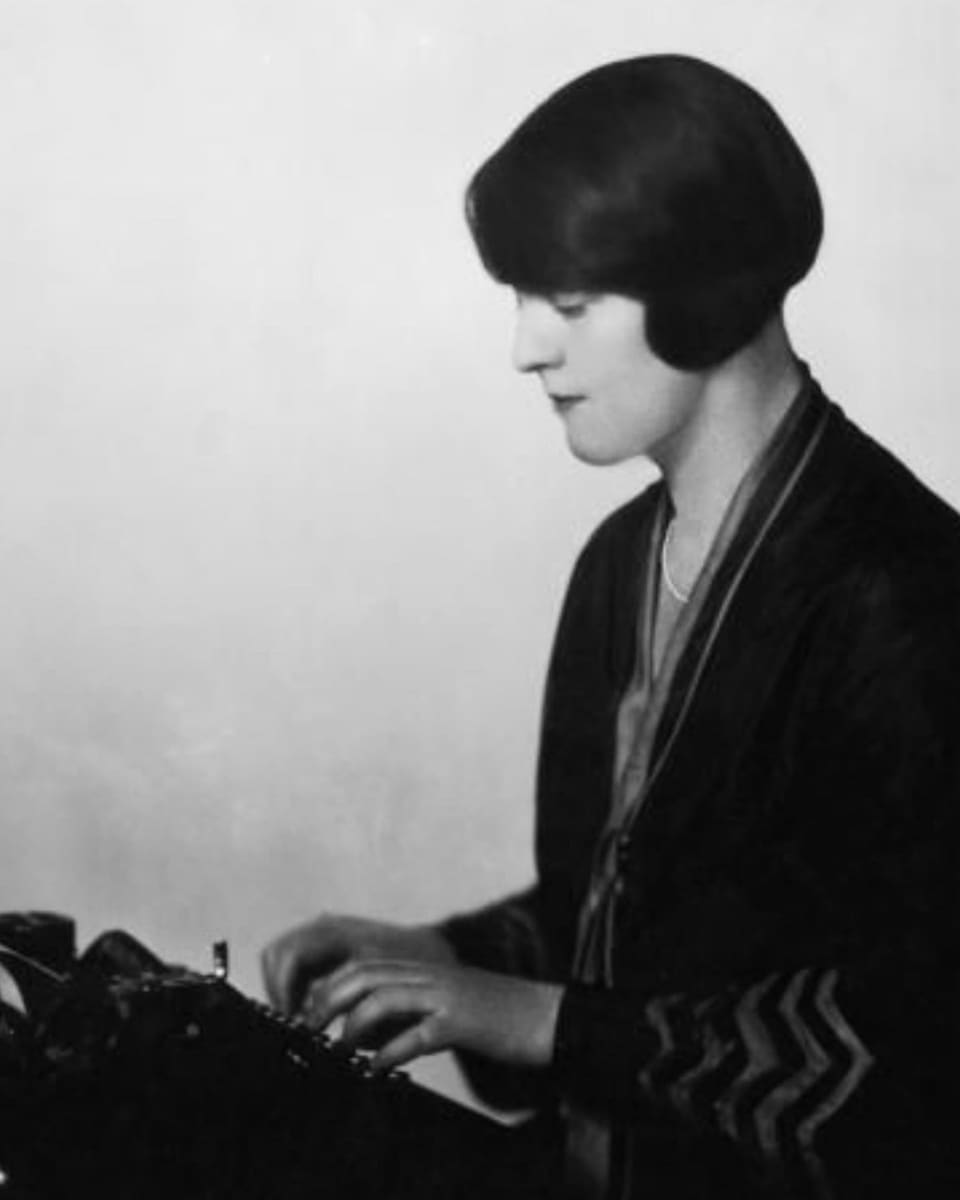 Eine schwarz gekleidete Frau, schreibend an der Schreibmaschine