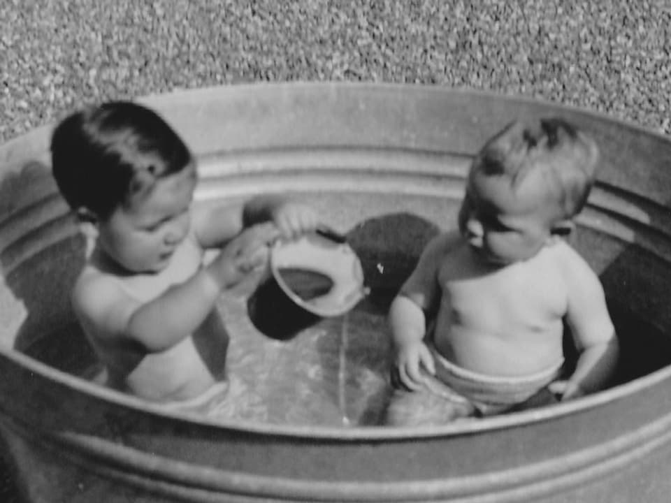 Zwei kleine Kinder sitzen in einer grossen silbernen Wäschetonne.