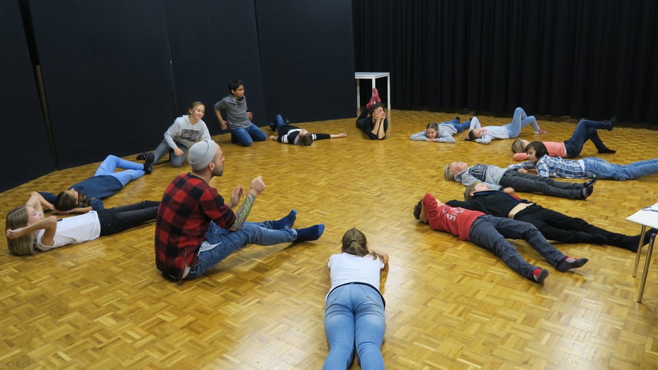 Kinder liegen in einem grossen Raum im Kreis formiert auf dem Boden.